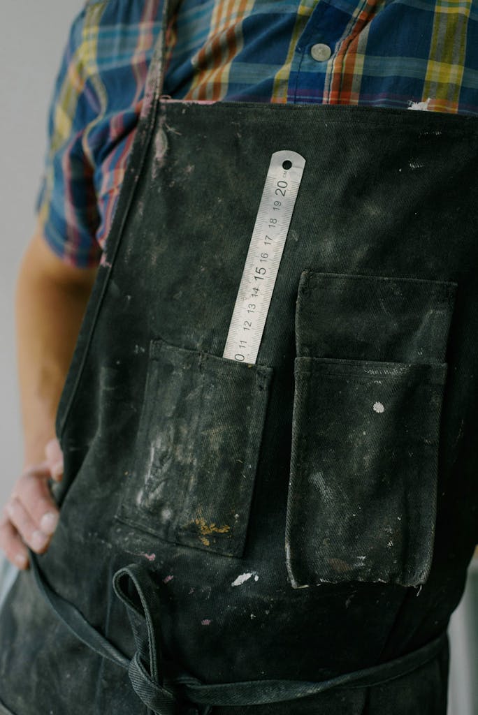 Crop anonymous male worker wearing overall with ruler in pocket during renovation works in apartment